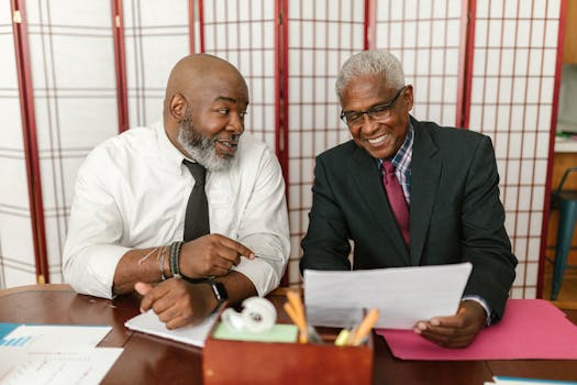 Two senior men in business attire discussing documents with a positive interaction in an office setting.