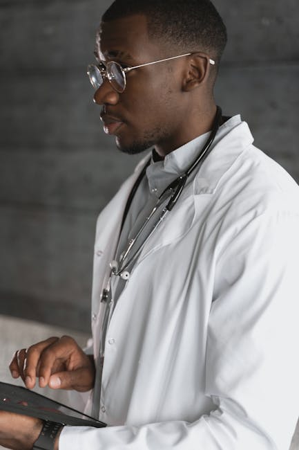 Focused African American doctor in lab coat using a tablet in a clinical setting.